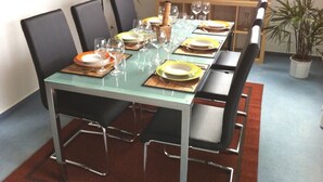 Mesa de jantar posta com pratos, copos e talheres, cercada por cadeiras.
