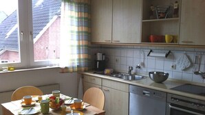 Cozinha com mesa de jantar posta para dois, lava-louças, forno e janela com cortinas.