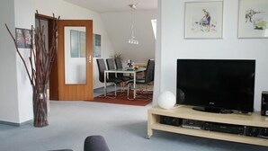 Uma sala de estar moderna com televisão de tela plana, área de jantar com mesa e cadeiras, e obras de arte nas paredes.