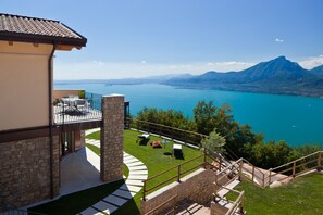 A modern house with a stone exterior, a balcony with outdoor furniture, and a view of a lake and mountains. - Villa Coloniale – Stunning Views & private heated pool (no share) (San Zeno di Montagna)