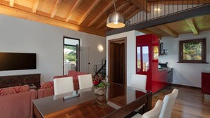 Un espace de vie moderne avec un plafond en bois, un coin repas doté d’une table en verre, des touches de couleur rouge et un espace cuisine.