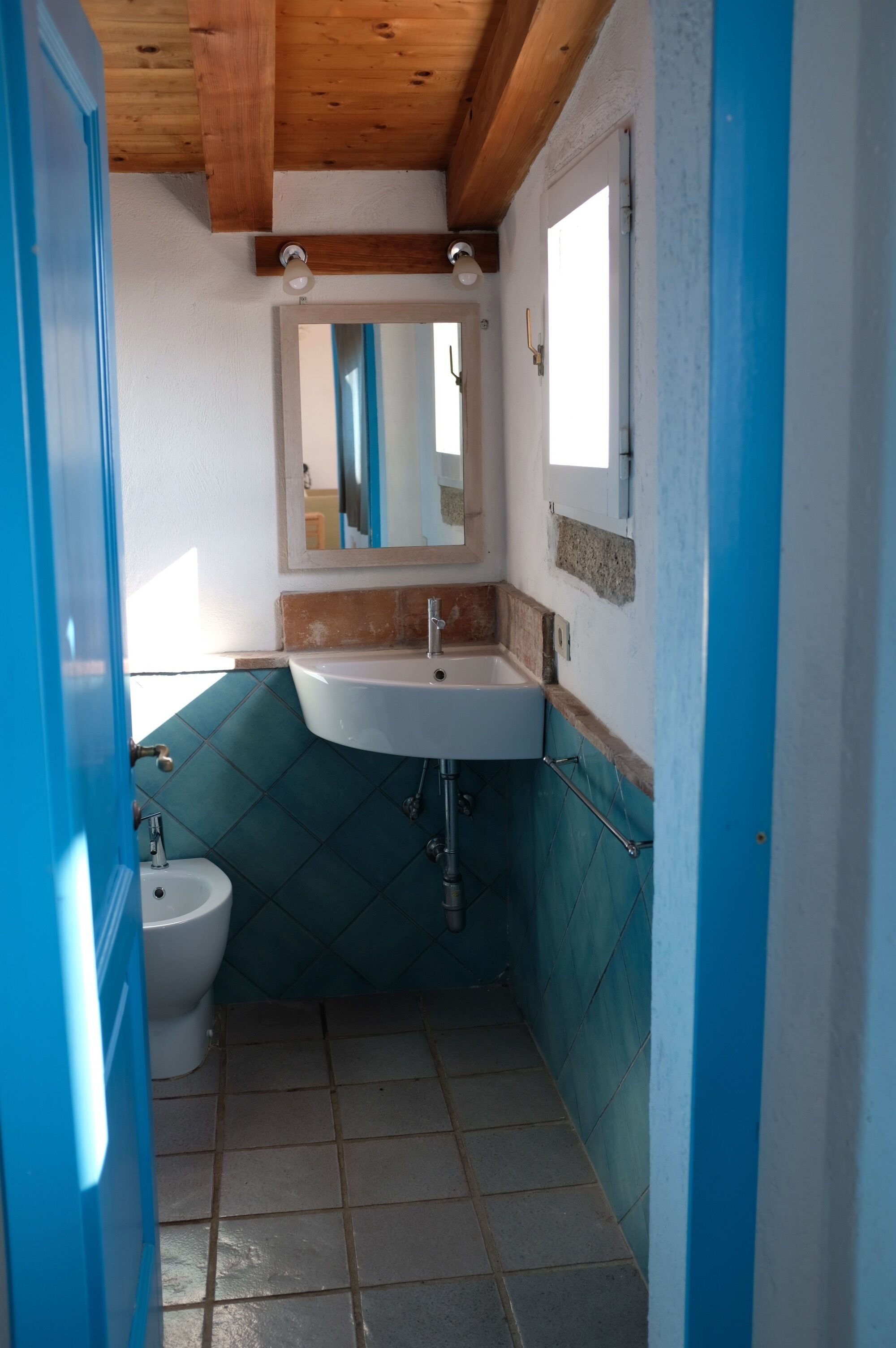 A narrow bathroom with a white sink, a mirror, and a blue door.