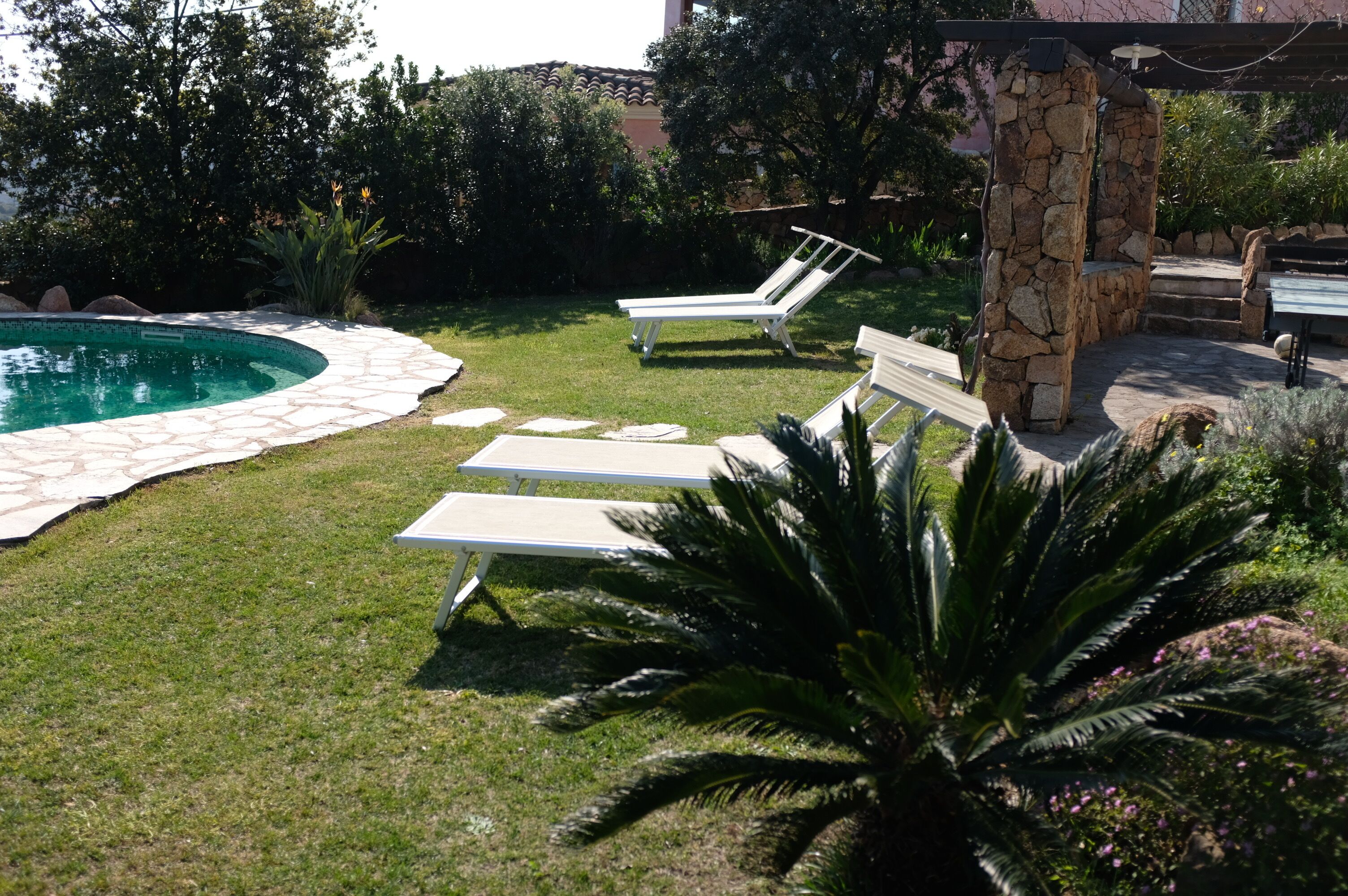 A backyard with a swimming pool, two lounge chairs, a stone pillar, and a stone bench.