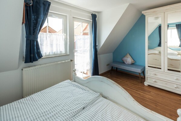 Een slaapkamer met een bed, een raam met gordijnen, een bankje en een dressoir.