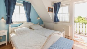 Un dormitorio con cama, dos mesitas de noche, una ventana con cortinas, un radiador y vistas al exterior.