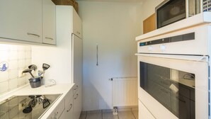 Una cocina compacta con armarios blancos, microondas, horno y cocina integrada.