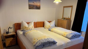 Una cama doble con ropa de cama floral, una mesita de noche con lámpara, un aparador de madera y un cuadro de una puesta de sol en la pared.