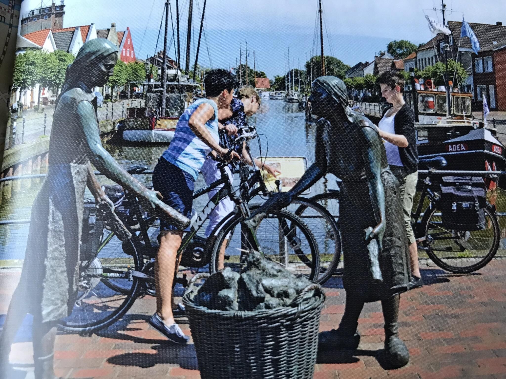 A sculpture of a person with a bicycle, a basket, and a bicycle parked on a cobblestone path.
