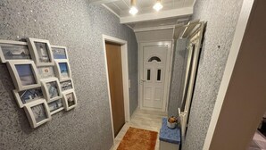 Un pasillo con pared gris texturizada, alfombra marrón y una puerta con ventanal circular.