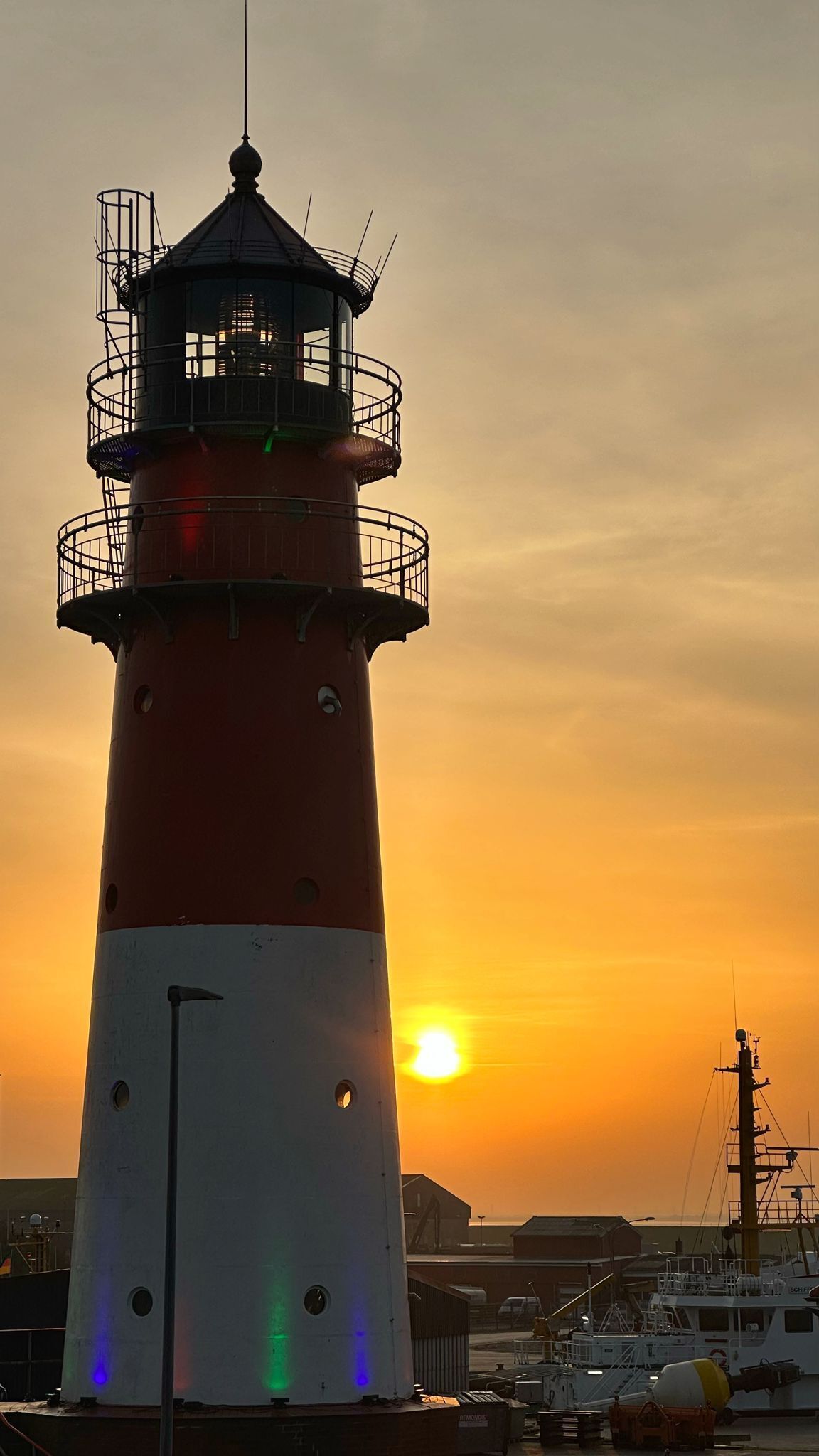 Een vuurtoren met een rood-wit gestreepte constructie, een balkon en een ondergaande zon op de achtergrond.