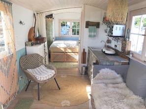 Ein gemütliches, rustikales Schlafzimmer mit Bett, Korbsessel, einem flauschigen weißen Sofa und einer kleinen Küchenzeile.