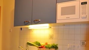 A kitchen with a microwave, a sink, and a basket of vegetables.