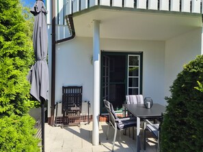 An outdoor patio with a table and chairs, a covered seating area, and a door leading to an interior space.