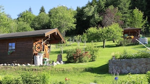 Eine Holzhütte mit einem großen Holzrad, umgeben von einer Steinmauer und üppigem Grün.