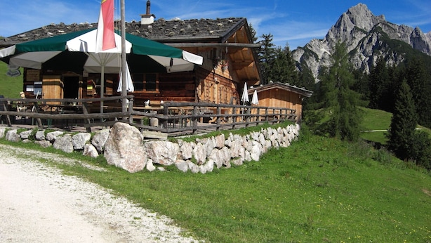 Eine Holzhütte in den Bergen mit Steinmauer und einer Flagge.