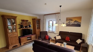 Ein Wohnzimmer mit einem dunklen Sofa, einem Holzschrank, einer TV-Konsole und einem Bild an der Wand.