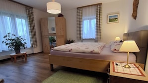 Ein Schlafzimmer mit einem hölzernen Bett, einem grünen Teppich, einem Holzschrank und einem Fenster mit Vorhängen.