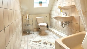 A small bathroom with a toilet, sink, and bathtub. There is a skylight above the toilet and a small window with a plant.