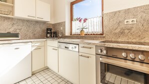 A kitchen with white cabinets, a dishwasher, a stove, and a window with a view of flowers.