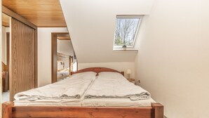 A bedroom with a sloped ceiling, a skylight, a wooden bed frame, and a view of a bathroom.
