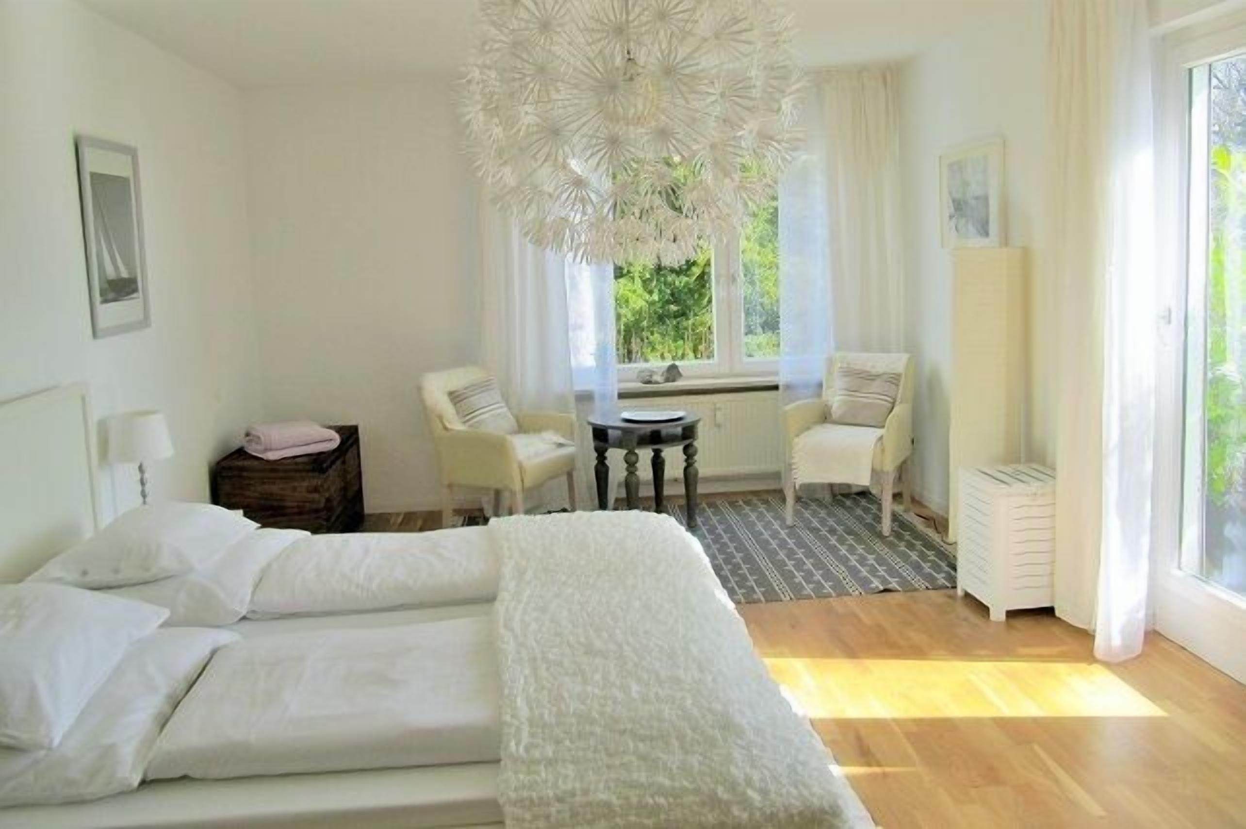 A bedroom with a bed, a chair, a table, and a window with curtains.