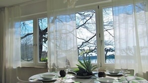 A dining area with a table set for four, large windows with sheer curtains, and a view of trees and sky. - Enjoy holidays in a prime location in Konstanz, the holiday in the south right on the shore (Konstanz)