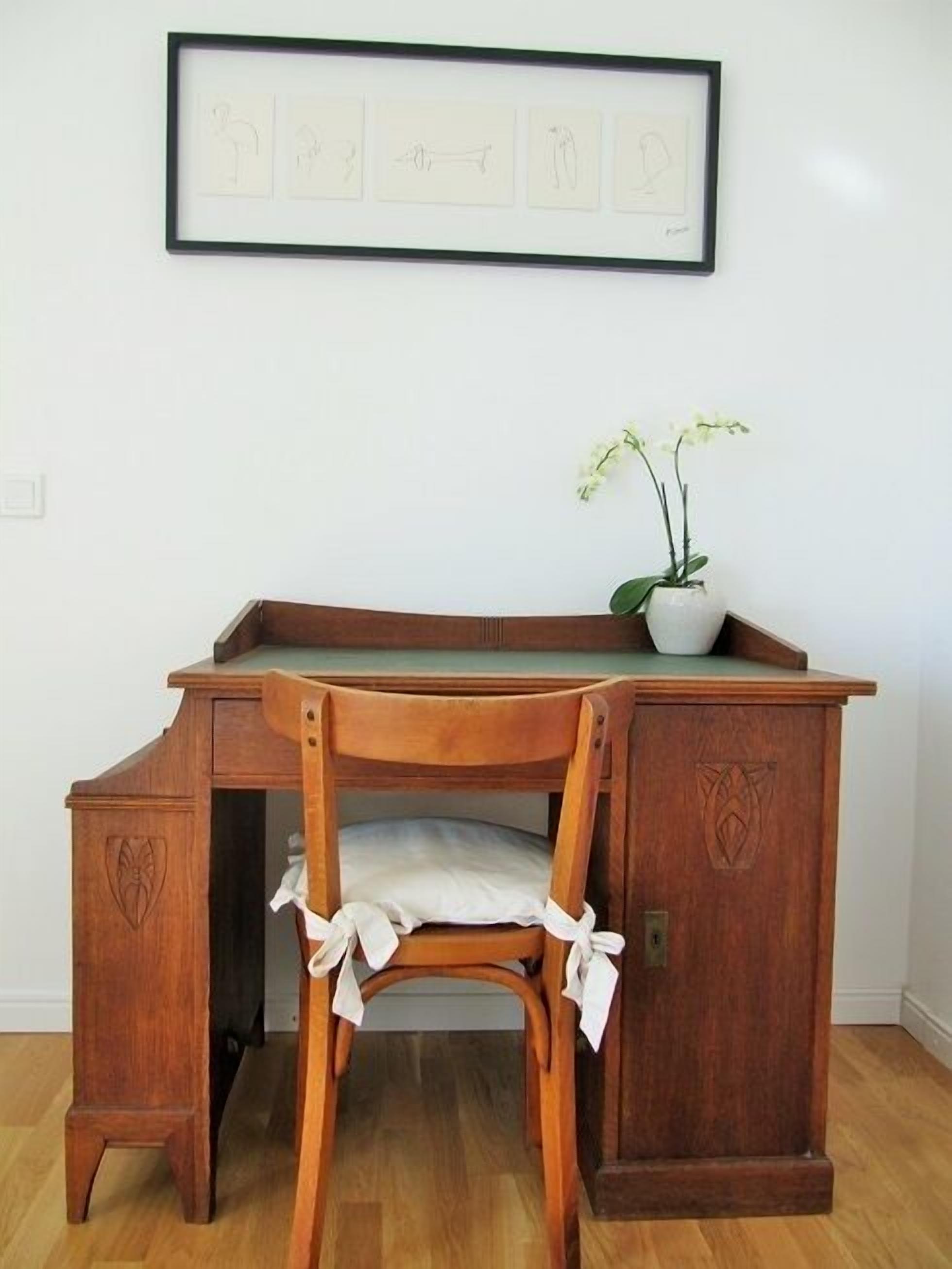 Una scrivania in legno con una sedia, un quadro incorniciato sopra e un'orchidea in vaso sulla scrivania.