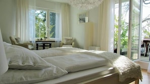 A bedroom with a large bed, a desk, and a chair. There is a window with curtains and a view of greenery outside. - Enjoy holidays in a prime location in Konstanz, the holiday in the south right on the shore (Konstanz)