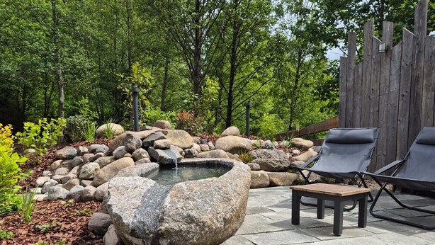 A garden with a hot tub, surrounded by rocks and trees. - Harzer Wiesenbaude - Holiday home with sauna and hot tub in a secluded location. (Braunlage)