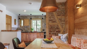 A rustic kitchen with wooden cabinets, a large wooden table, and a hanging copper light fixture. - Harzer Wiesenbaude - Holiday home with sauna and hot tub in a secluded location. (Braunlage)