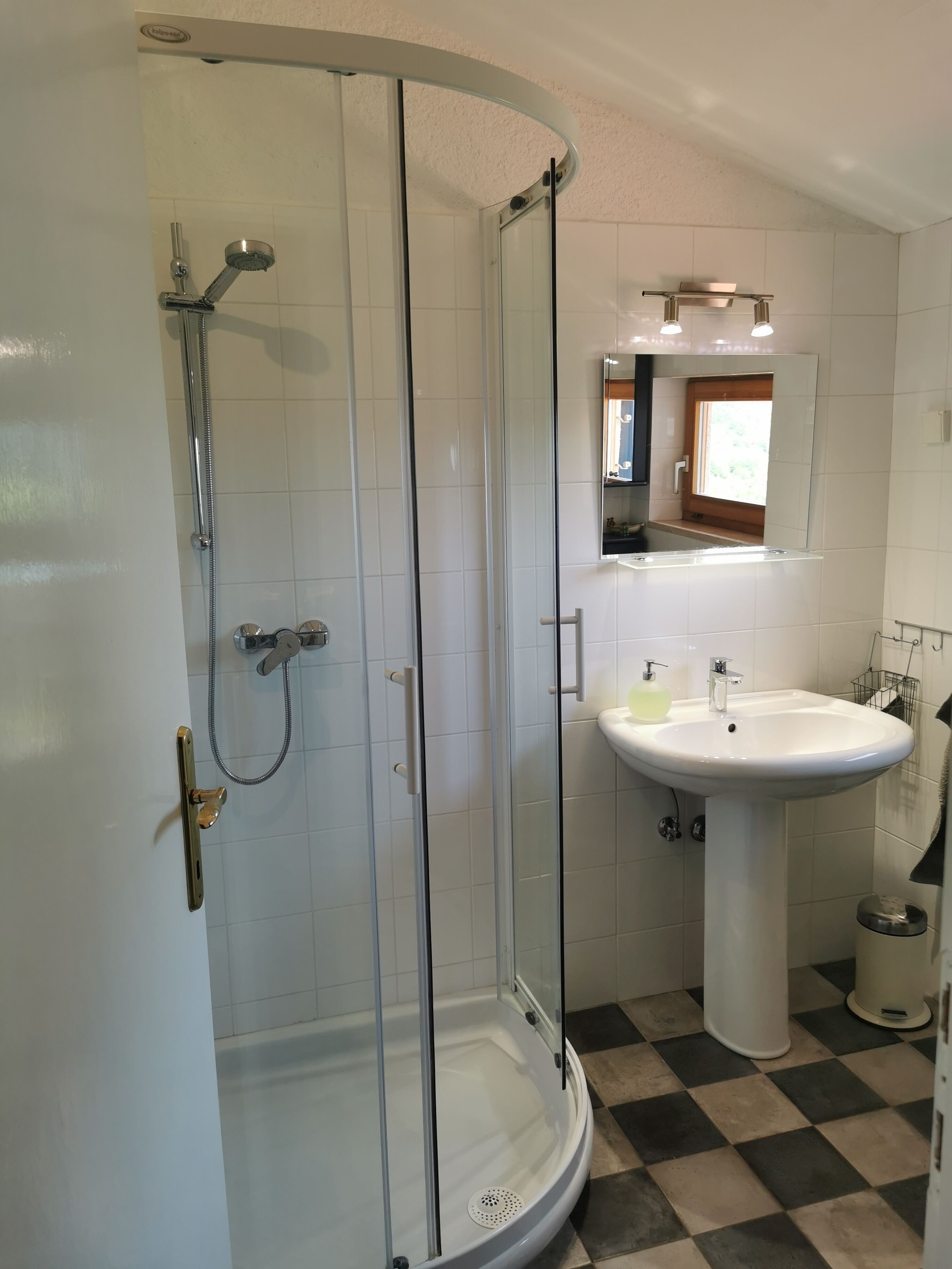 A bathroom with a glass-enclosed shower, a pedestal sink, and a mirror above the sink.