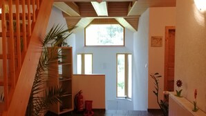 Un interior espacioso con una escalera de madera, un ventanal grande y un suelo de baldosas.