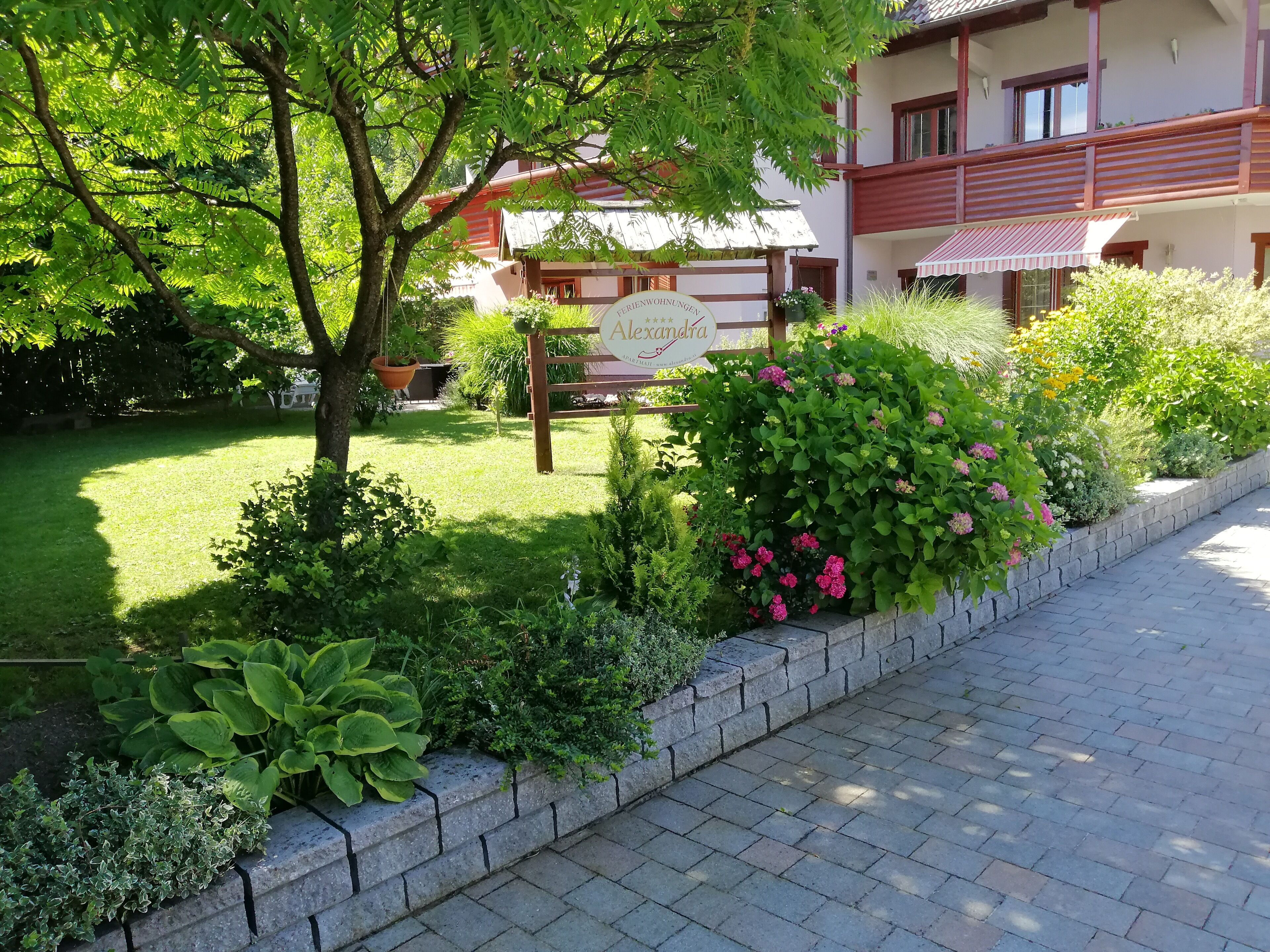 Un jardín bien cuidado con diversas plantas y un cartel que indica una propiedad llamada 'Alexandra'.