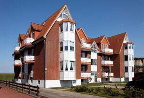 Un edificio residencial de varios pisos con fachada de ladrillo, múltiples balcones y cielo despejado.