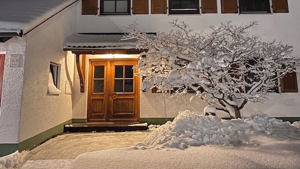 A two-story wooden house with a snow-covered roof and a wooden door.