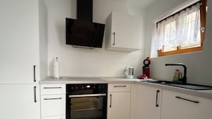A kitchen with white cabinets, a black oven, a window with lace curtains, and a wooden floor.
