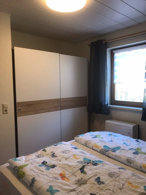 A room with a bed, a wardrobe, a window with curtains, and a radiator.