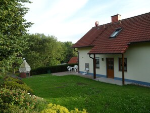 A house with a red-tiled roof, a covered patio with white chairs, and a well-maintained garden.