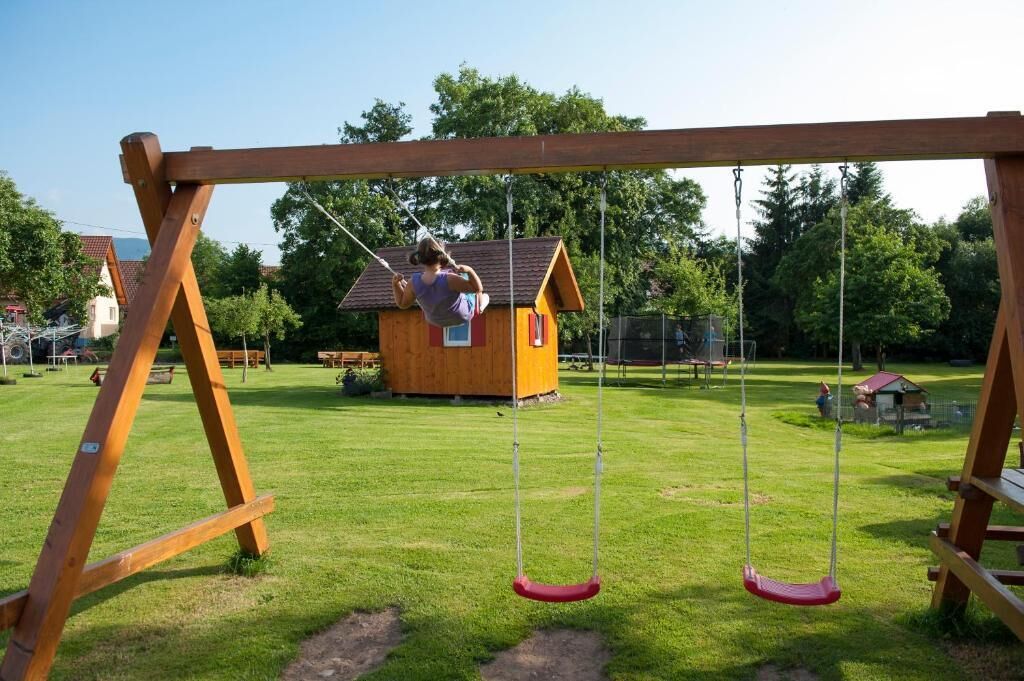 A wooden swing set in a park with a small wooden house in the background.