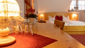 Een hotelkamer met een houten bed, een rode tafelkleed met dessin, een lamp en een vaas met bloemen.