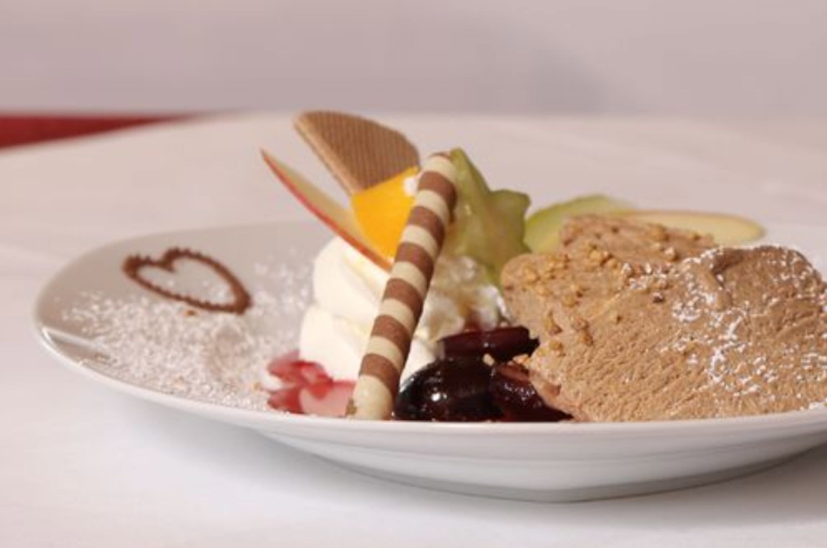 Une assiette de desserts comprenant divers éléments, notamment une gaufrette enrobée de chocolat, de la crème fouettée et une part de gâteau.