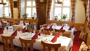 Een restaurant met houten tafels en stoelen, rode servetten en een klok aan de muur.