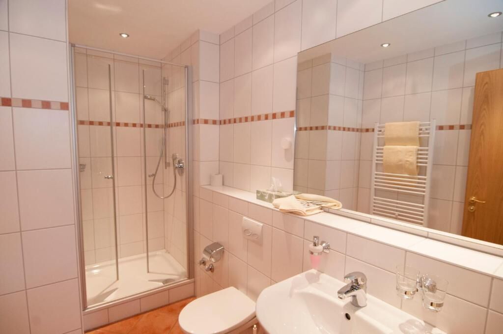 Een moderne badkamer met een douchecabine van glas, een witte wastafel en een grote spiegel.