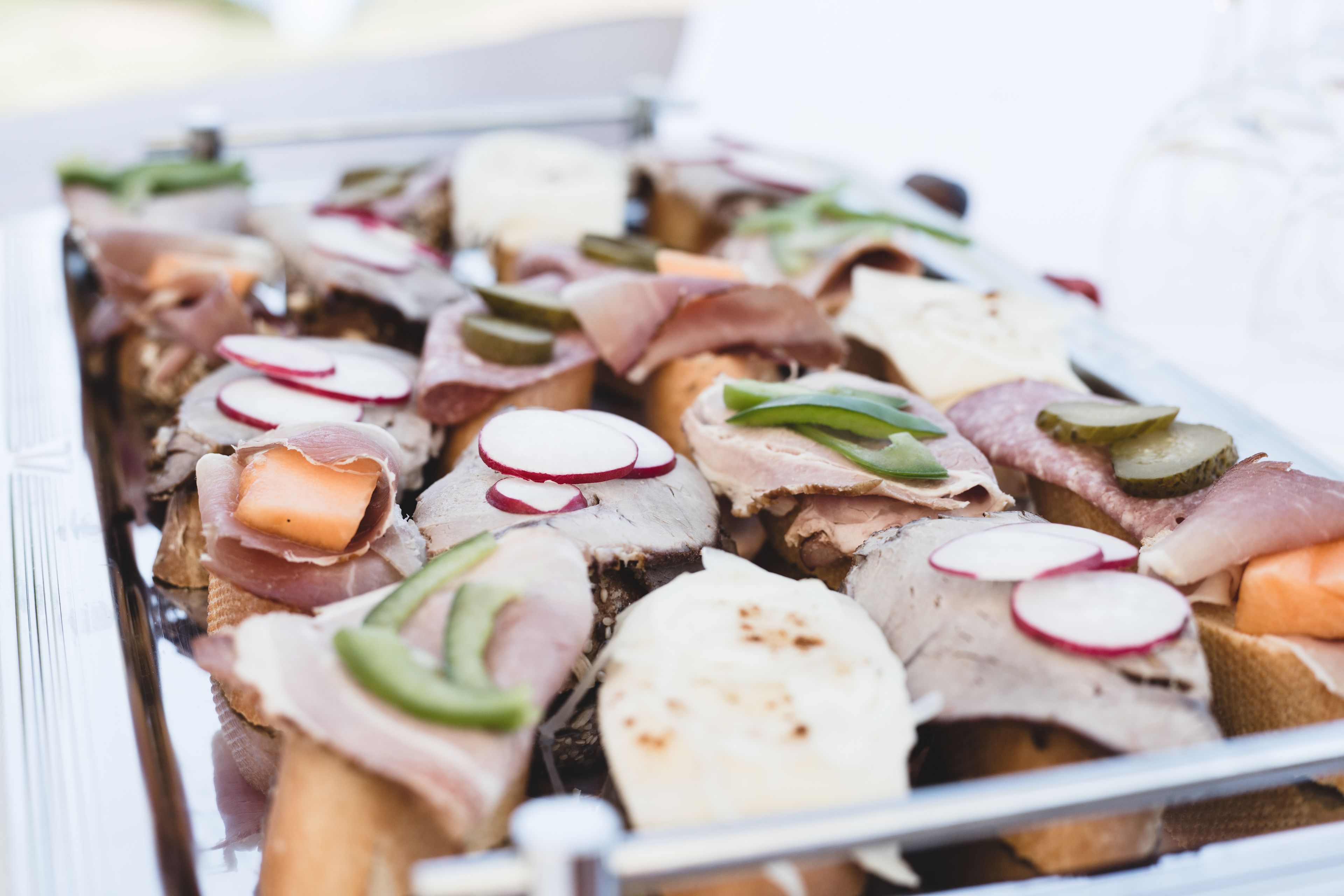 A tray of assorted meats and cheeses, including ham, salami, and possibly prosciutto, garnished with radishes and green peppers.
