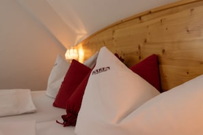 A hotel room with a wooden headboard, white and red pillows, and a lamp on the wall.