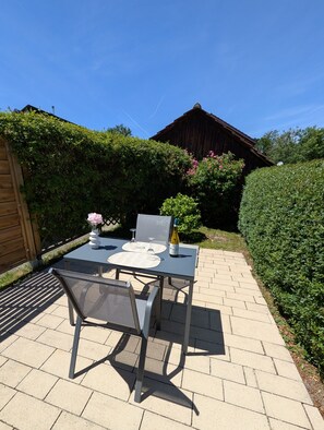An outdoor patio with a table and chairs, a bottle, and a vase with flowers.