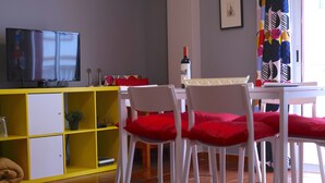 A dining area with a yellow cabinet, white chairs with red cushions, a white table, and a television on a stand. - Nice apartment 75 m from the sea (Arico)