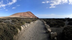 A desert landscape with a prominent hill, a dirt path, sparse vegetation, and a distant ship on the horizon. - Nice apartment 75 m from the sea (Arico)