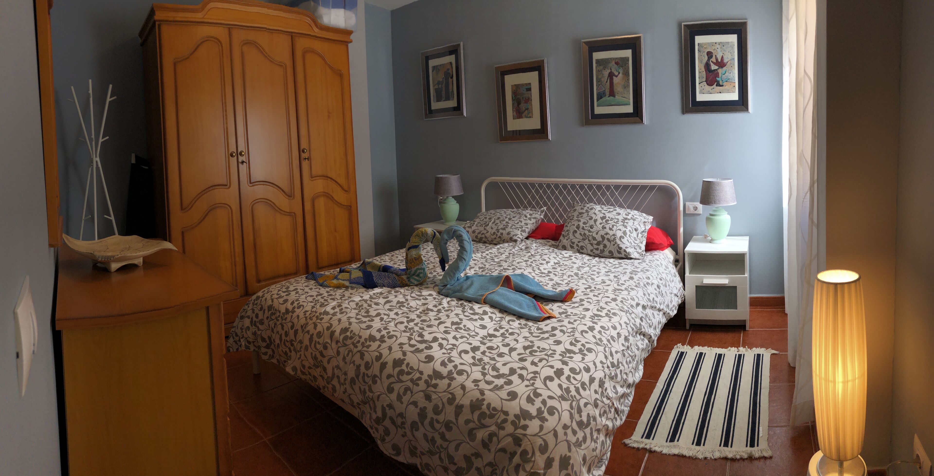 Une chambre à coucher comprenant un lit, une armoire, des tables de chevet, des lampes et des œuvres d’art accrochées au mur.