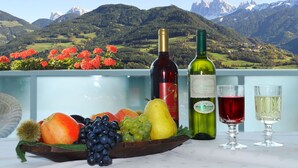 Una mesa con fruteros, botellas de vino y copas, con montañas al fondo.